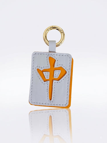 A rectangular leather keychain or luggage tag in the shape of a mahjong tile with the dragon symbol, attached to a gold metal key ring, shown on a reflective white background.