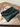 Green clutch bag with scalloped edge and gold charm on a book