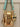 Gold metallic handbag with a cat-shaped keychain on a neutral background
