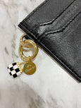 Black leather wallet with gold and silver charm on a marble surface