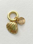 Gold charm with shell design and round tag on a light gray background