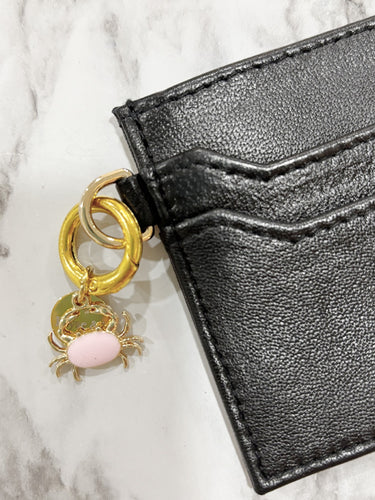 Black leather wallet with a gold and pink charm on a marble surface