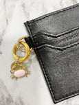 Black leather wallet with a gold and pink charm on a marble surface