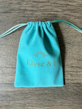 Turquoise drawstring pouch with 'Elyse & i' branding on a wooden surface