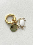 Gold charm with a white oval and round tag on a light gray background