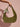 Green handbag with floral ribbon held by a hand against a pink background