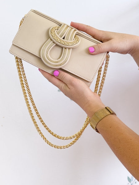 Beige handbag with gold chain held by a hand on a white background