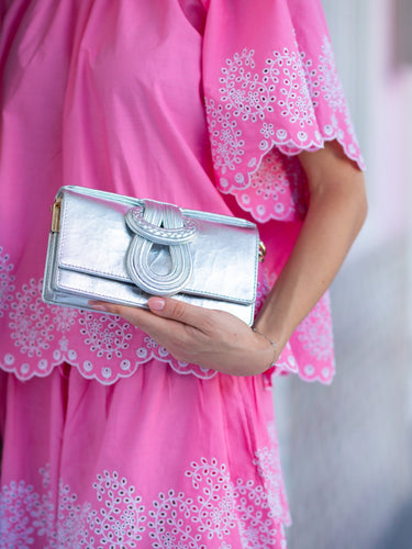 Silver clutch held by a hand wearing a pink dress with white floral embroidery.