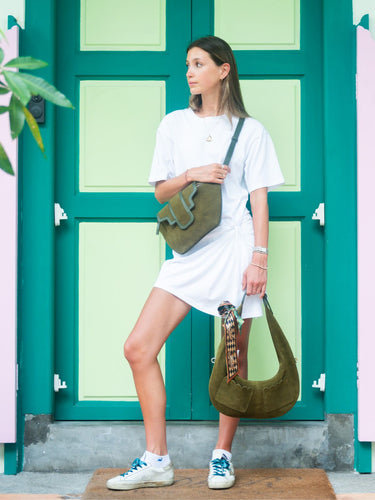 Woman holding a green handbag in front of a teal door