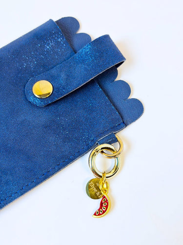 Blue suede glasses clutch with gold accents and a keychain on a white background