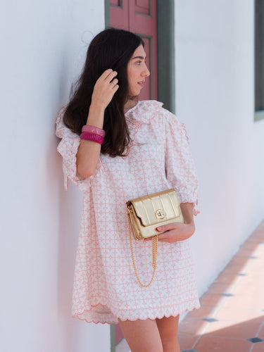 Woman in a white dress holding a gold Otis handbag from Elyse & i brand against a light-colored wall.