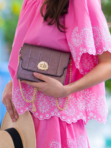 Person holding a mulberry metallic handbag from Elyse & i called Otis 
with a pink outfit and straw hat in the background