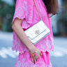 Person wearing a pink dress with white embroidery, holding a silver leather bag by Elyse & i called Otis shell. 