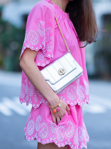 Person wearing a pink dress with white embroidery, holding a silver leather bag by Elyse & i called Otis shell. 