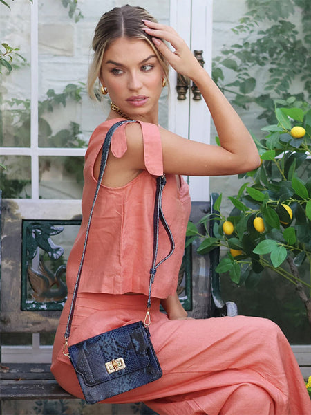 Woman in a peach outfit with a blue Elyse & i Otis handbag seated outdoors.