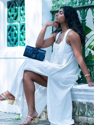 Woman in a white dress sitting on a bench with a blue Elyse & i Nell Knot clutch