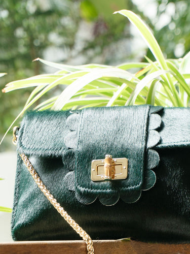 Green handbag with floral details and gold chain strap against a blurred plant background