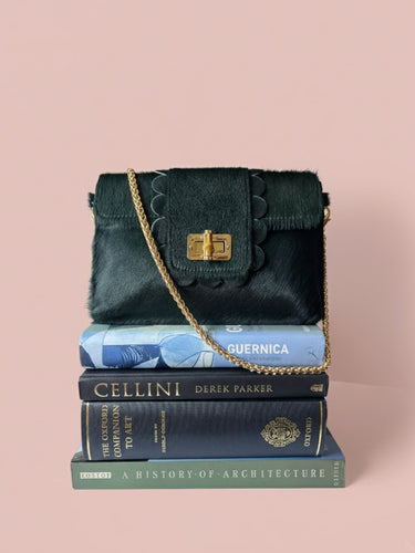 Green handbag with gold chain strap on a stack of books against a pink background