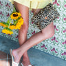 Person wearing a yellow checkered skirt, white sandals, and holding a leopard print clutch with sunflowers.