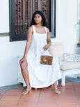 Woman in a white dress holding a cheetah print Finn Scallop clutch by Elyse & i on a tiled floor.