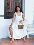 Woman in a white dress holding a cheetah print Finn Scallop clutch by Elyse & i on a tiled patio.