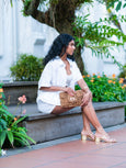 Woman sitting outdoors with a floral arrangement and plants in the background holding a cheetah print Finn Scallop clutch by Elyse & i.