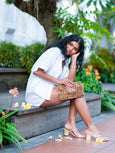 Woman sitting outdoors with a cheetah print Finn Scallop clutch by Elyse & i , surrounded by greenery