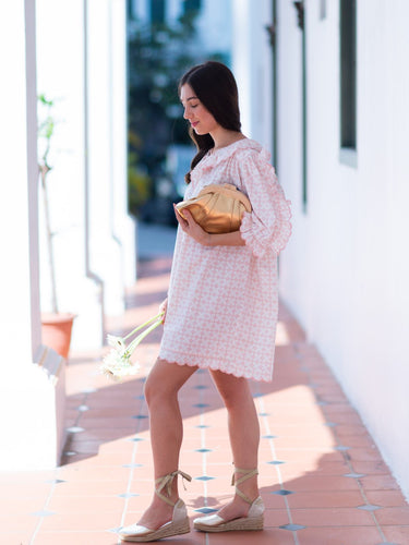 Woman in a white dress holding a Elyse & i Dawn Scallop clutch on a sunlit outdoor path.