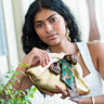 Woman holding a Elyse & i Dawn Scallop clutch with decorative elements indoors