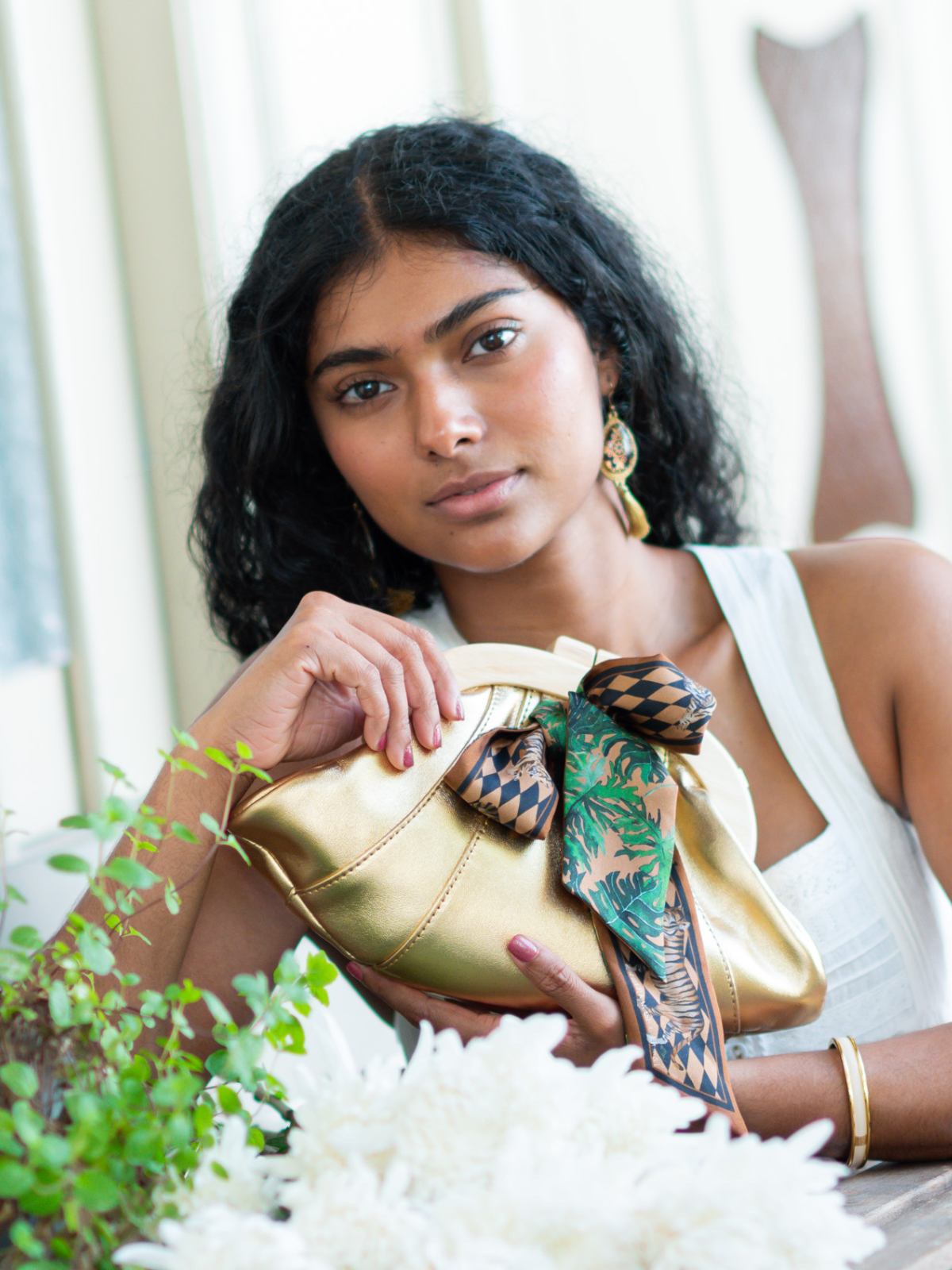 Woman holding a Elyse & i Dawn Scallop clutch with decorative elements indoors