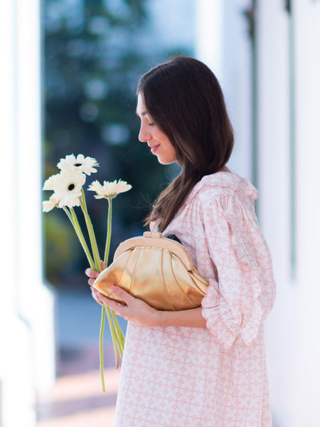 Woman holding a bouquet of flowers and a gold Elyse & i Dawn Scallop clutch outdoors