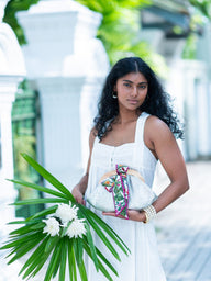 Woman in a white dress holding a floral arrangement with a blurred background, carrying a silver croco embossed leather Dawn Scallop bag with bow by Elyse & i