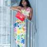 Woman in a colorful dress holding a red Elyse & i Finn Scallop clutch on a white railing.