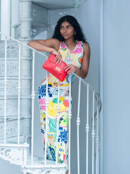 Woman in a colorful dress holding a red Elyse & i Finn Scallop clutch on a white railing.