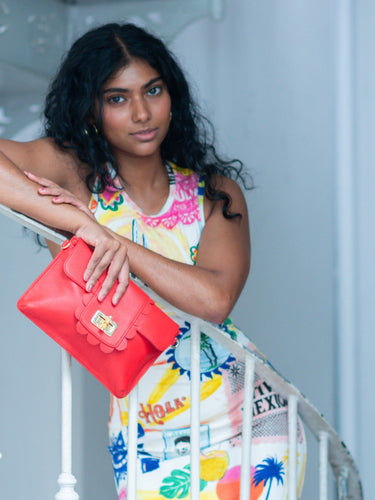 Woman holding a red Elyse & i Finn Scallop handbag with a colorful dress in an indoor setting
