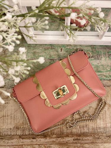 Pink Elyse & i Finn Scallop handbag with gold accents on a wooden surface with flowers in the background