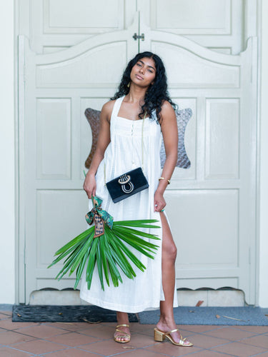 Woman in a white dress holding green leaves wearing Elyse & i Nell Knot bag in black and gold, worn as a sling bag with chain.  