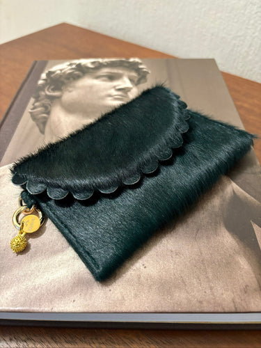 Green clutch bag with scalloped edge and gold charm on a book