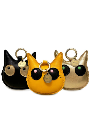 Three cat-shaped keychains in black, yellow, and gold on a white background