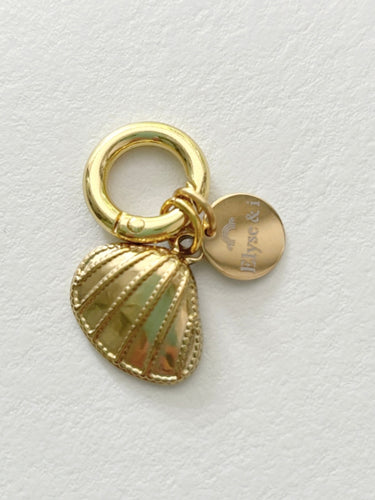 Gold charm with shell design and round tag on a light gray background