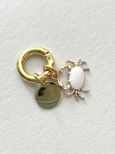 Gold charm with a white oval and round tag on a light gray background