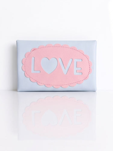 A light blue leather tissue holder with a pink scalloped oval patch on the front featuring the word 'LOVE' with a heart replacing the 'O'.