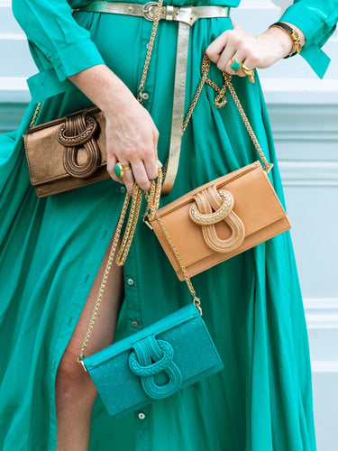 Person holding two handbags, one gold and one green, against a blurred background.