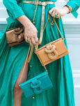 Person holding two handbags, one gold and one green, against a blurred background.