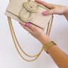 Beige handbag with gold chain held by a hand on a white background