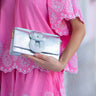 Silver clutch held by a hand wearing a pink dress with white floral embroidery.