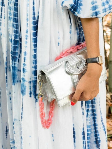 Person holding a silver clutch with pink chain strap, wearing a blue and white patterned outfit.