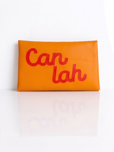 An orange rectangular leather tissue holder with the words 'can lah' printed in red script across the front, set against a clean white background with a soft reflection below.