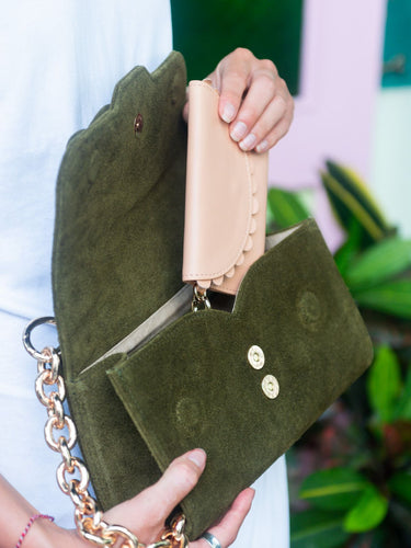 Green clutch with a chain strap held by a hand against a blurred background