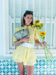Woman in a yellow outfit holding sunflowers and a gray handbag against a decorative wall.